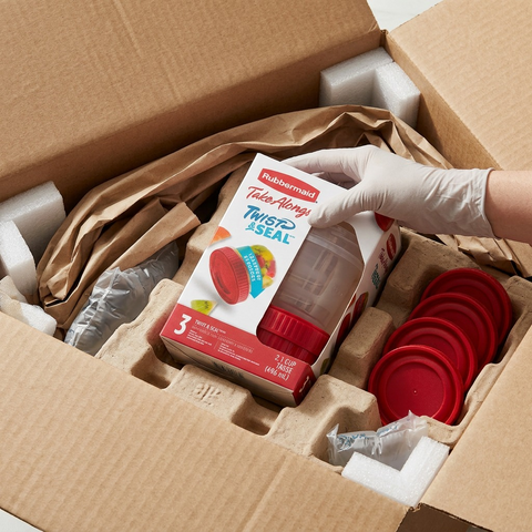A premium close-up photo shows one intact Rubbermaid TakeAlongs 3-pack nested inside protective paper pulp in an open shipping box.